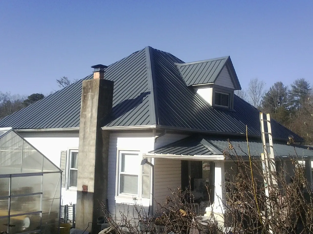Dark blue standing seam metal roof on a white farmhouse with dormer — Slate & Tile Roof Repair by Roofing Brothers in Monaca