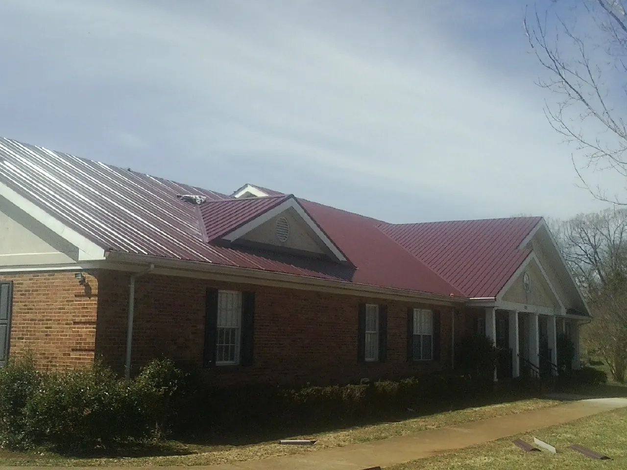 Red metal roof with gabled entries on a long brick building, from a Hail Damage Roof Repair job in Monaca