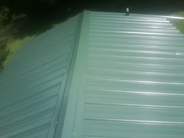 New green metal panels meeting at the ridge of a roof — Flat Roof Repair work by our crew in Monaca