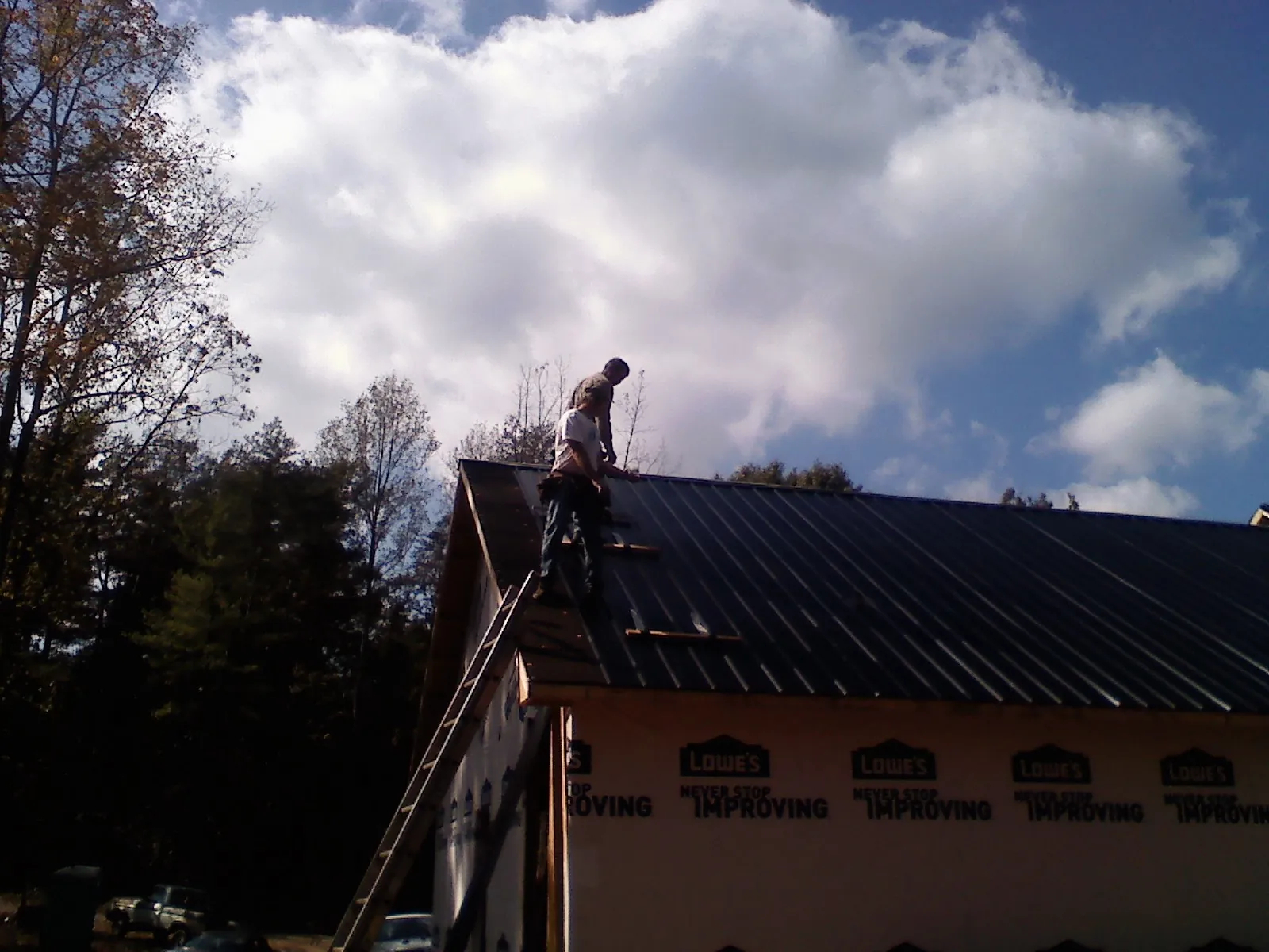 Roofer fastening dark metal panels high against a cloudy sky, from a Roof Inspection job in Monaca